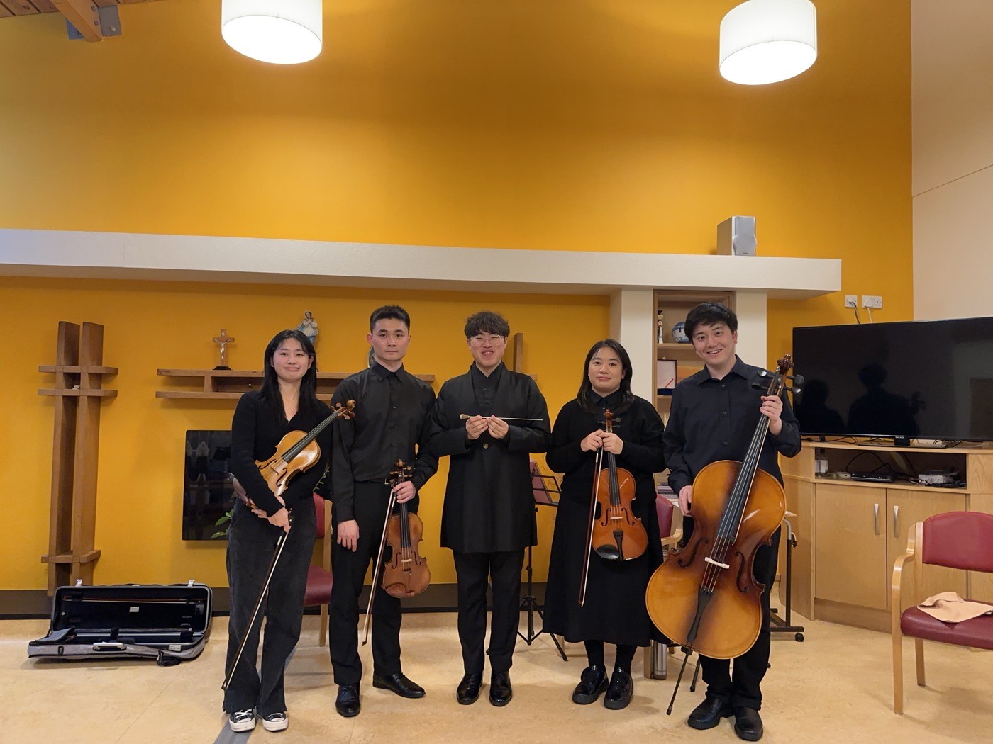 Four string players of the Letters Ensemble and their conductor in a bright yellow room